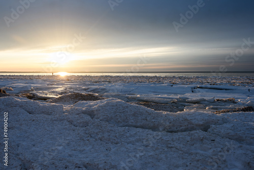 The Baltic Sea coast at the end of winter. The seashore covered with broken ice floes  in the evening golden sunlight. Bright sun in a cloudy hazy sky. Backlight