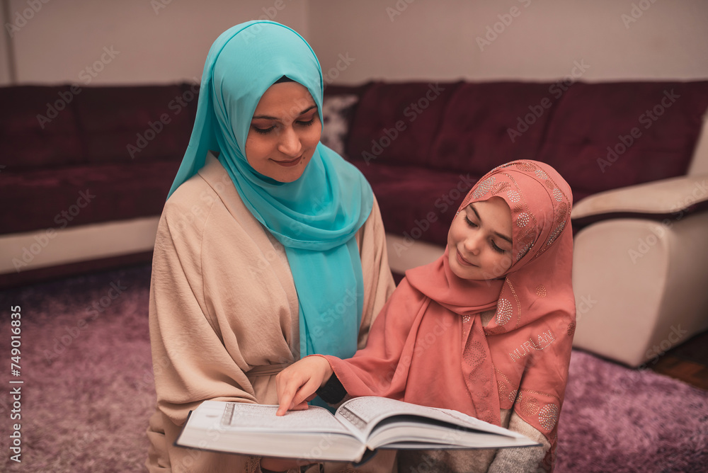 Traditional Muslim woman and her little girl with hijab reading Quran at home