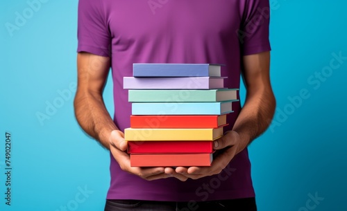 man holding stacked up book against blue background