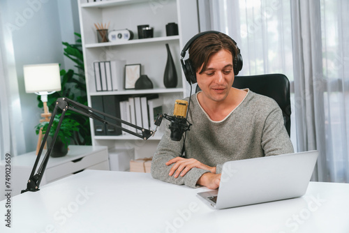 Host channel in smiling smart broadcaster recording  talking show with script and smartphone on desk on live social media  wearing headphones to record video streamer at modern home studio. Pecuniary.