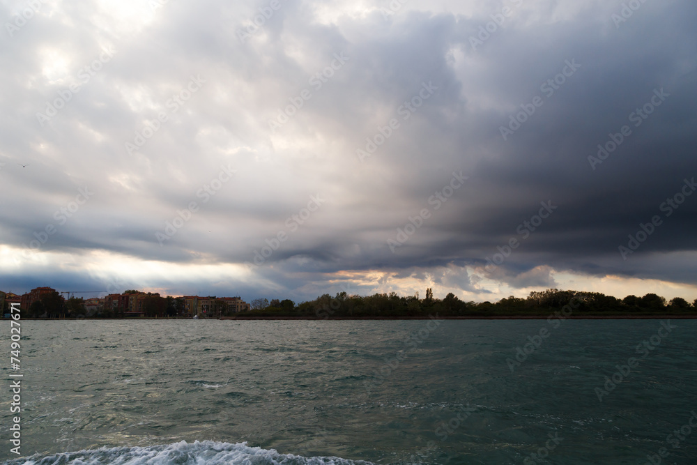 Venice, Italy. Giudecca and Sacca San Biagio islands in Venetian Lagoon with dark blue stormy sky in background. View from water bus.