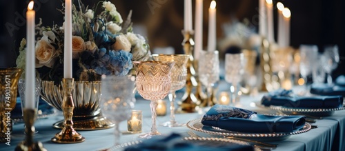 A banquet table adorned with an opulent display of candles, plates, and luxurious decor. The setting exudes elegance with gold and blue elements complementing the warm glow of the candles. © Emin