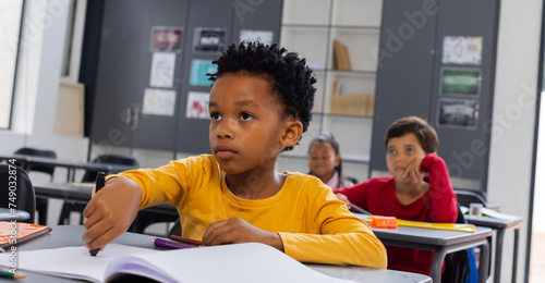 Fotografie Biracial boy in a yellow shirt looks attentive in a school classroom