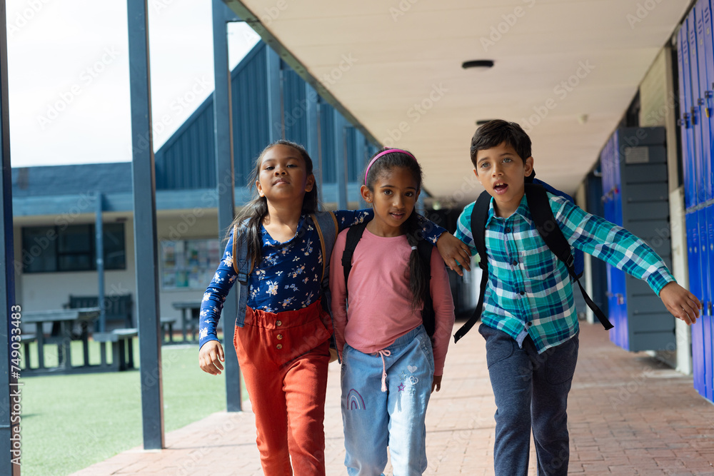 Obraz premium Three biracial children walk through a school corridor with lockers