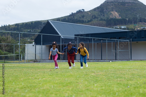 Three biracial girls are playing on a grassy field at school, with copy space