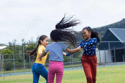 Three girls are joyfully holding hands and spinning in a grassy field in school