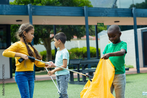 Slika na platnu Biracial girl in a yellow top assists an African American boy with collecting tr