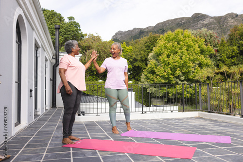 Senior African American woman and biracial woman high-five during yoga outdoors with copy space
