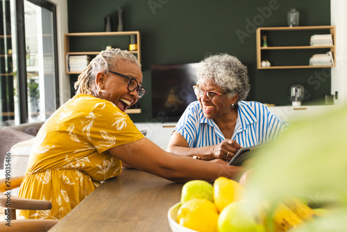 Senior African American woman and senior biracial woman share a laugh over a tablet at home