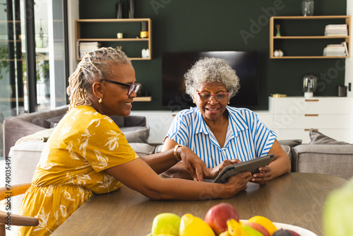 Senior African American woman and senior biracial woman are sharing a tablet in a cozy living room a