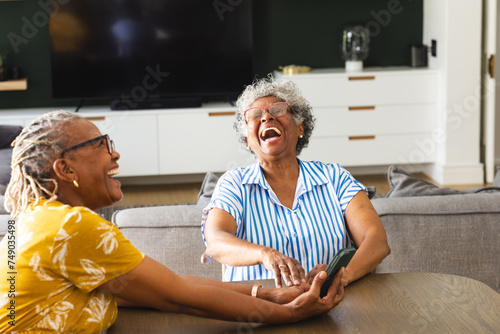 Senior African American woman and senior biracial woman share a laugh together on a couch at home