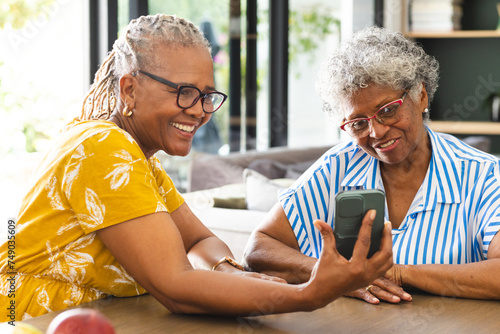 Senior African American woman and senior biracial woman share a moment over a smartphone at home