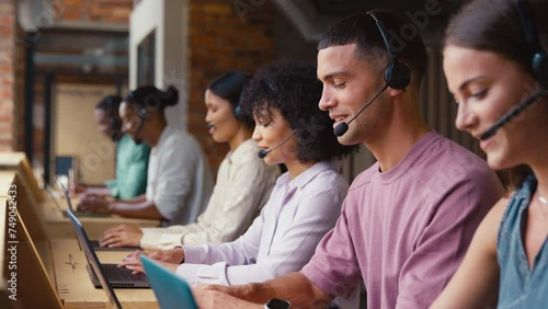 Multi-Cultural customer support or telesales team in modern open plan office wearing headsets and talking with customers - shot in slow motion photo