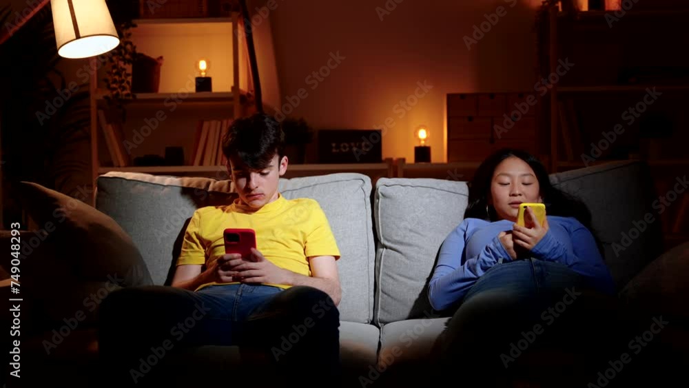 Bored teenager couple using phone on sofa. Social media addiction concept Bored teenager couple using phone on sofa. Social media addiction concept
