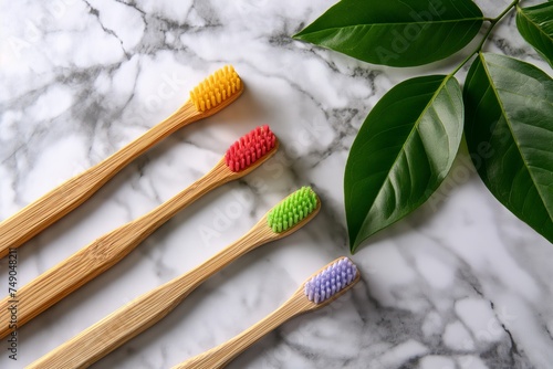 Colorful wood toothbrushes and green leaves on bright marble table  flat lay