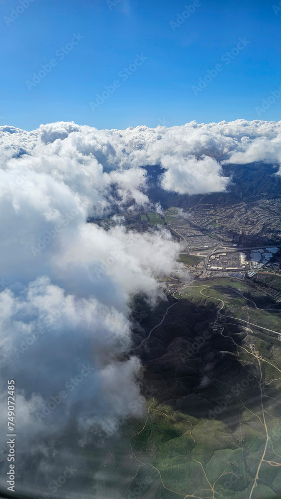 Fototapeta premium An aerial shot of southern California with vast buildings of homes and office buildings, majestic mountain ranges and blue sky with clouds in California USA