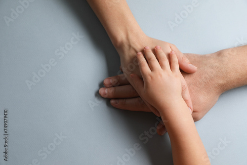 Parents and child holding hands together on gray background, top view. Space for text