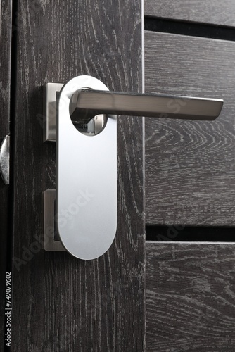 Closed wooden door with blank hanger on metal handle, closeup photo