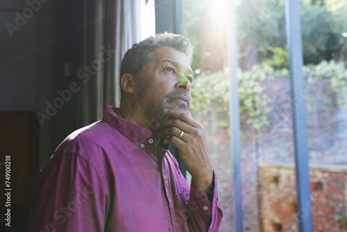 Senior biracial man with greying hair appears pensive, hand on chin, gazing out