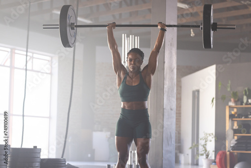 Strong biracial woman lifts a barbell overhead in a gym photo
