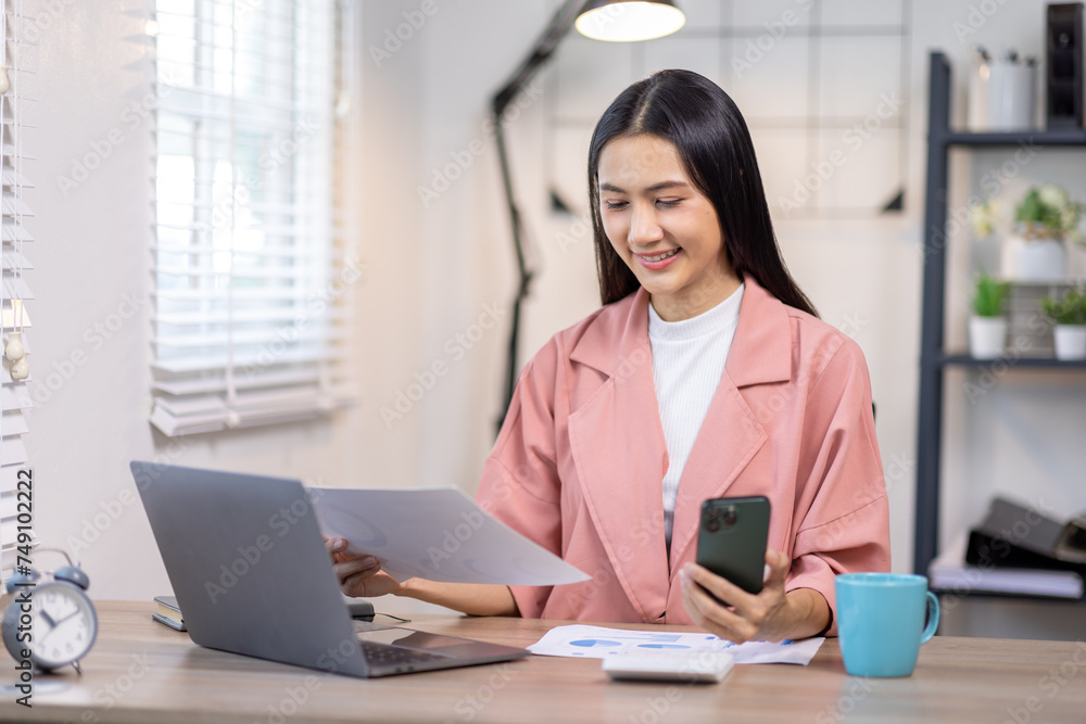 Portrait of happy young asian woman accountant working documents on laptop and phone desk using calculator for calculate finance report in home office Portrait of happy young asian woman accountant working documents on laptop and phone desk using calculator for calculate finance report in home office