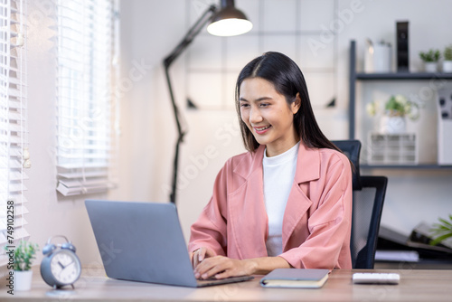 Portrait of happy young asian woman accountant working documents on laptop and phone desk using calculator for calculate finance report in home office
