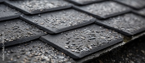 A detailed black and white close-up of a tiled roof, showcasing the textured stone coated bituminous coating providing protection against moisture and rain. The pattern of the tiles is visible