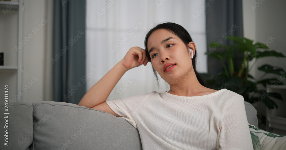Selective focus, Relaxed young woman wear wireless headphones enjoying rest sitting on sofa in living room listening to music at home Selective focus, Relaxed young woman wear wireless headphones enjoying rest sitting on sofa in living room listening to music at home