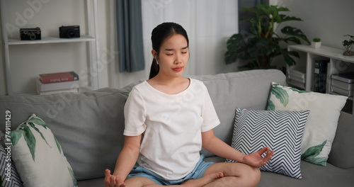 High angle view, Happy young woman wear wireless headphones meditating doing a lotus pose at home with eyes closed, relaxing body and mind alone on sofa in the living room,relaxation lifestyle