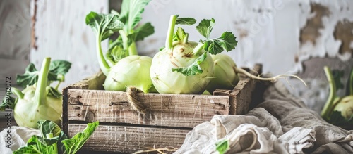 A wooden crate filled with just picked kohlrabi with leaves is placed on top of a table against a white backdrop. photo