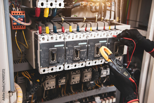 Electricity and electrical safety maintenance service system, Technician hand checking electric current voltage at circuit breaker terminal and cable wiring in main power distribution board. photo