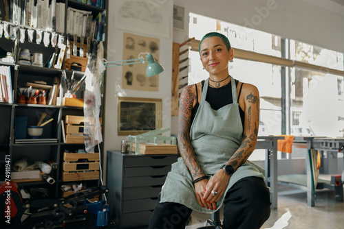 Smiling female designer sitting on background of own workshop and looks camera