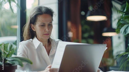 ฺฺBusiness woman working in office checking documents. Mid aged businesswoman accounting manager executive or lawyer using laptop reading paper file financial report, tax invoice