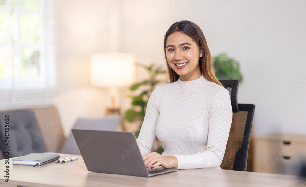 Beautiful young asian business woman working on her laptop in her home office. Beautiful young asian business woman working on her laptop in her home office.