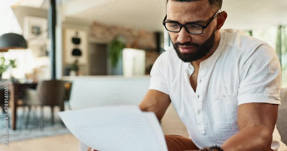 Man, serious and finance documents on sofa with reading for savings, debt or crisis in home living room. Person, paperwork and stress for loss, thinking and fail with loan, mortgage or taxes in house Man, serious and finance documents on sofa with reading for savings, debt or crisis in home living room. Person, paperwork and stress for loss, thinking and fail with loan, mortgage or taxes in house
