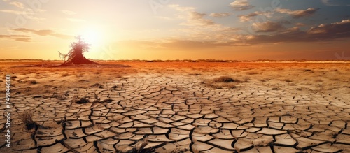 The image shows the sun slowly descending on a barren area, highlighting the desolate landscape with dry soil and scarce vegetation. The scene captures the harsh reality of drought, heat, and water