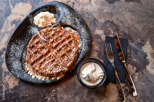 Marble Chocolate Waffle with chocolate, whipped cream, knife and fork served in dish isolated on dark background top view cafe dessert food