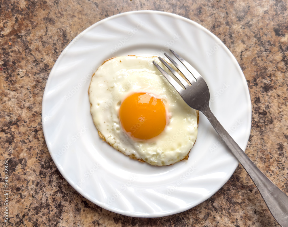Fried egg on a white plate with a fork on the table Fried egg on a white plate with a fork on the table