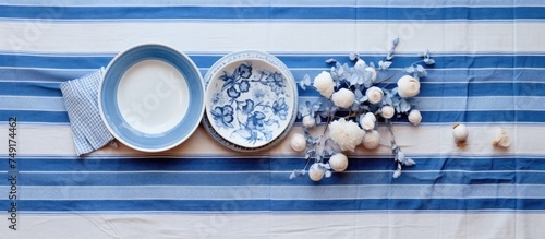 A top-down view of a table covered with a classic blue and white tablecloth. Plates and flowers are arranged neatly on top, creating an elegant setting. photo