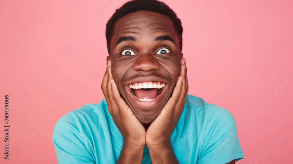 close-up of a young man with a joyful and surprised expression, hands on his cheeks, against a vibrant pink background. close-up of a young man with a joyful and surprised expression, hands on his cheeks, against a vibrant pink background.
