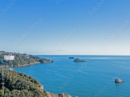An aerial drone photograph of Meadfoot and Tor Bay in Torquay Devon with a view of the blue sea and blue sky and shag rock, thatcher's rock and ore stone in the distance photo