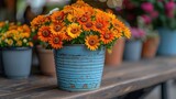 a blue vase filled with orange flowers on top of a wooden table in front of potted plants on top of a wooden table.