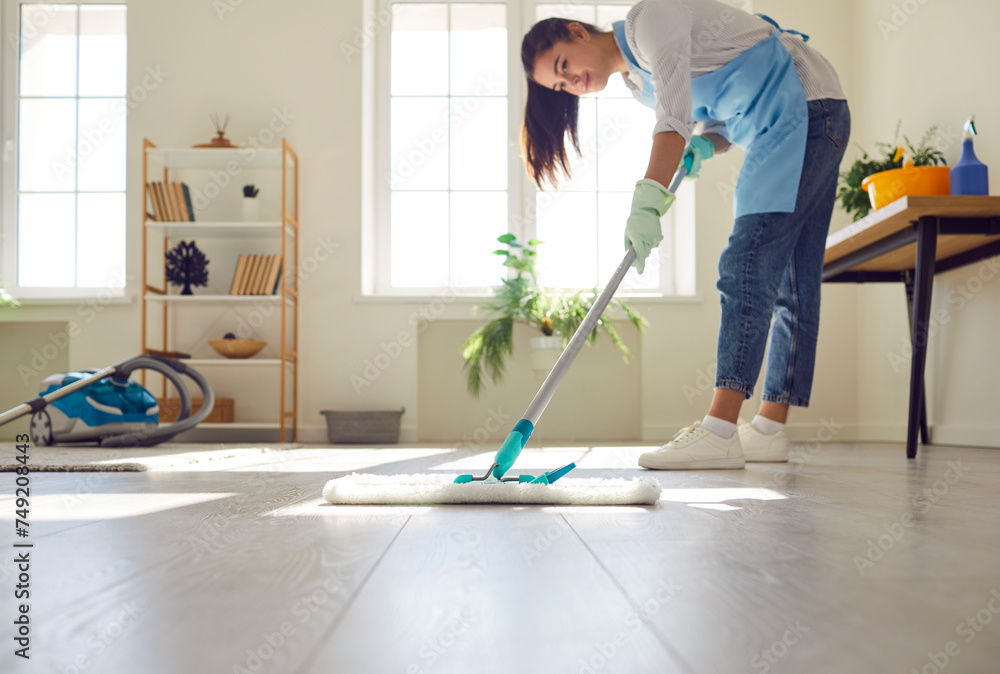 Woman maid takes charge with a mop, showing household care, mopping the living room floor. Epitomizes the art of cleaning as a service, showcasing the woman commitment to maintaining a pristine home. Woman maid takes charge with a mop, showing household care, mopping the living room floor. Epitomizes the art of cleaning as a service, showcasing the woman commitment to maintaining a pristine home.
