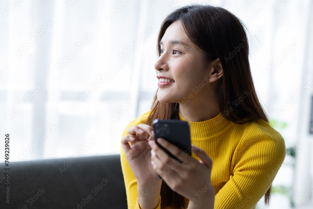 Happy young asian woman sitting on sofa using smartphone in living room at home. Happy young asian woman sitting on sofa using smartphone in living room at home.