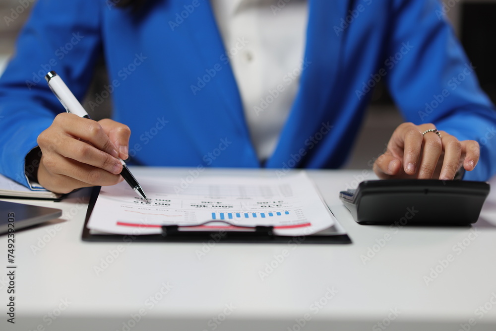 Fototapeta premium Businesswoman working overtime in office, she is analyzing financial figures data chart in business report document.