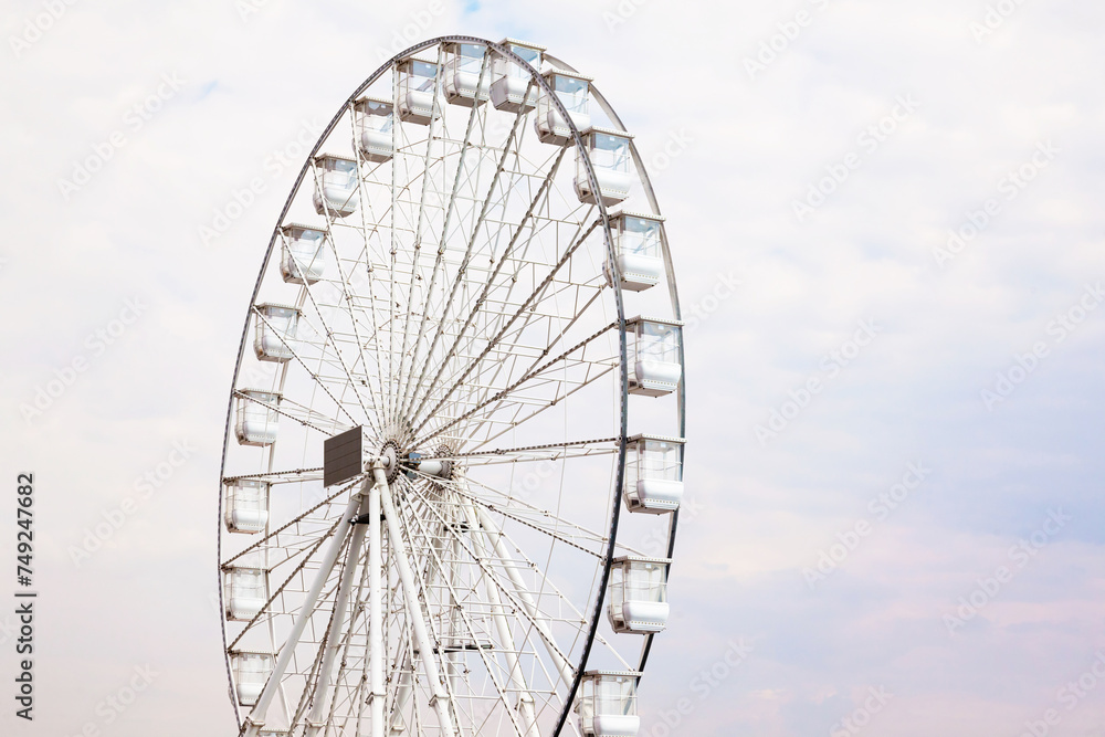 An empty Ferris wheel during the day against a white cloudy sky.