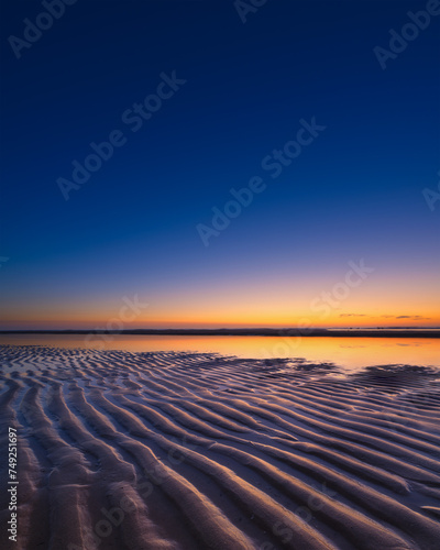 A seascape during sunset. Lines of sand on the seashore. Bright sky during sunset. A sandy beach at low tide. Wallpaper and background.