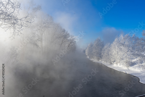 Foggy winter landscape with river and trees in hoarfrost