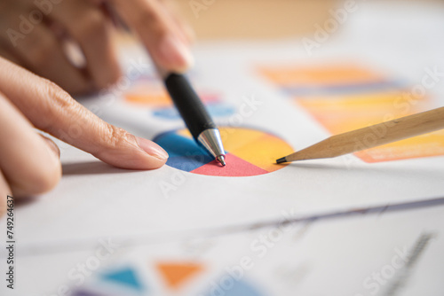 Close-up of a professional analyzing statistical data on a colorful pie chart report with a pen and pencil in hand.