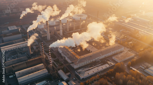 Aerial view of an industrial plant with smokestacks emitting vapor during sunset, showcasing the infrastructure and environmental impact.